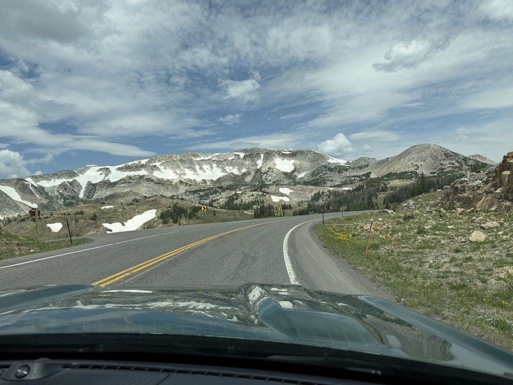 A view from the front seat of a car looking ahead at the snow-covered mountains.