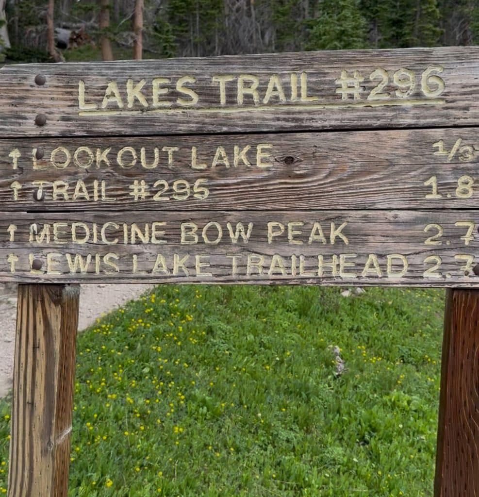 A close-up trailhead sign reads Lakes Trail #296 and has distances.