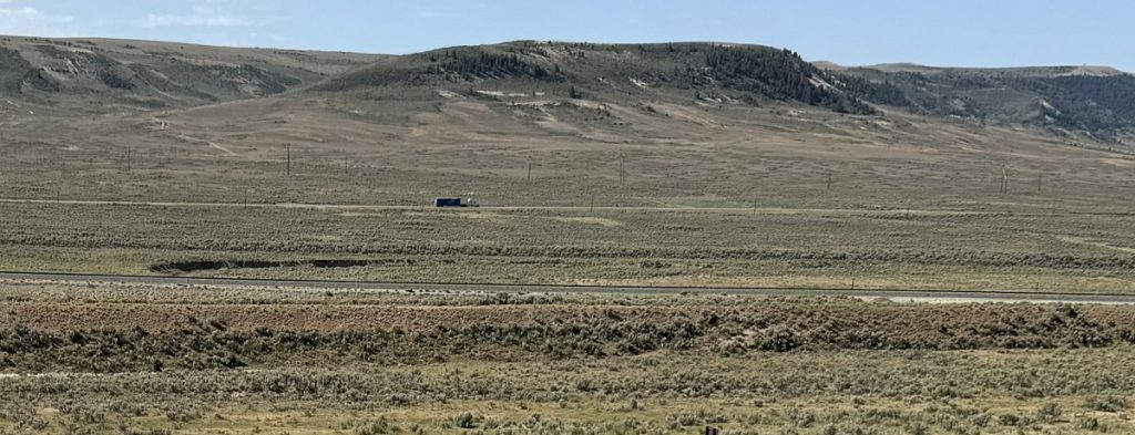 A barren landscape shows a truck on a road in the distance.