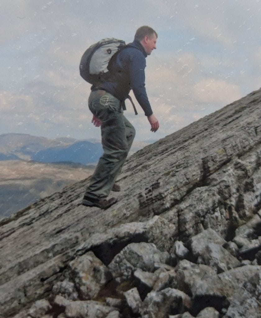 A hiker with a backpack takes steps up an steep rocky incline.