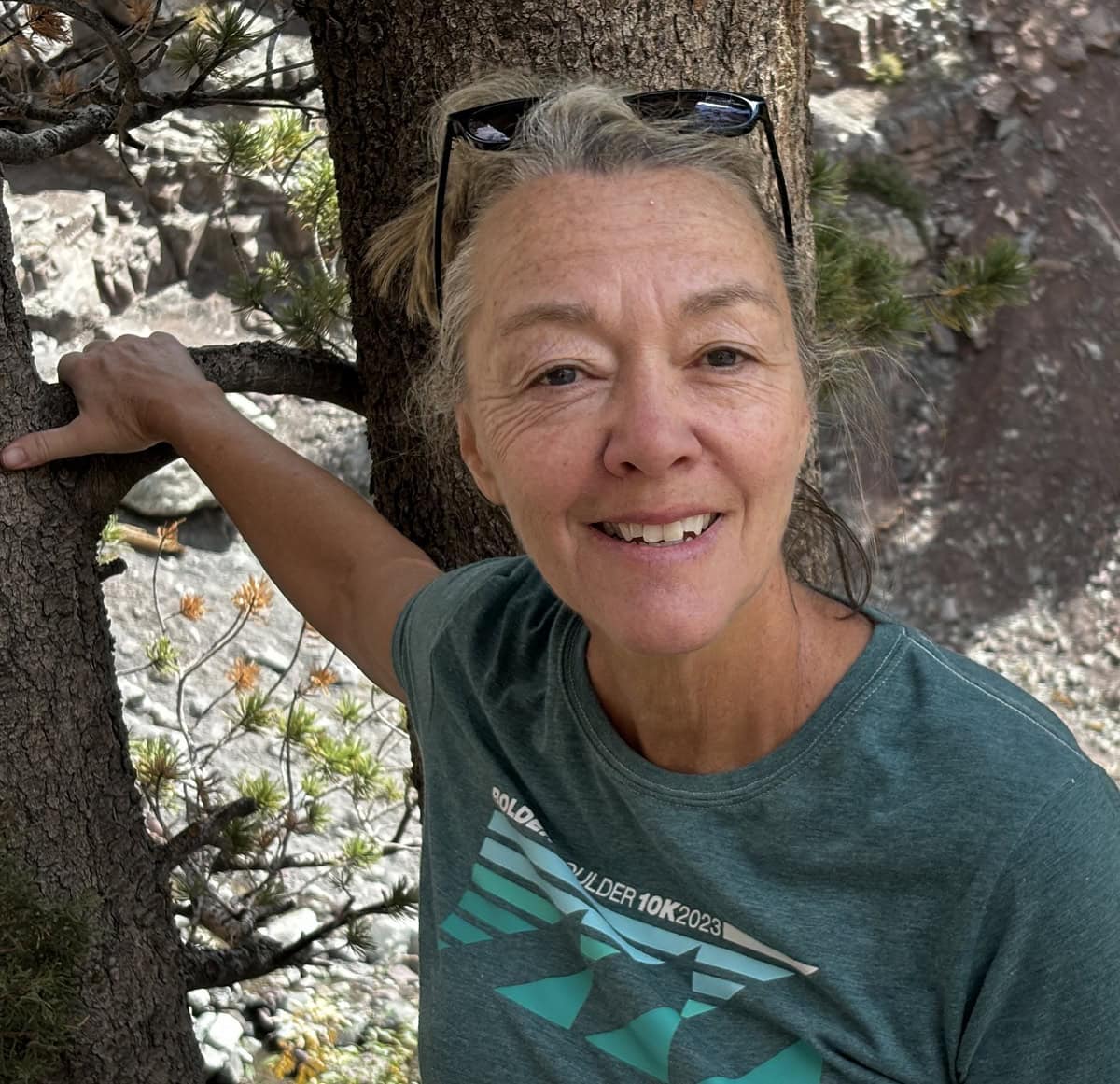 A woman in a green shirt leans up against a tree.