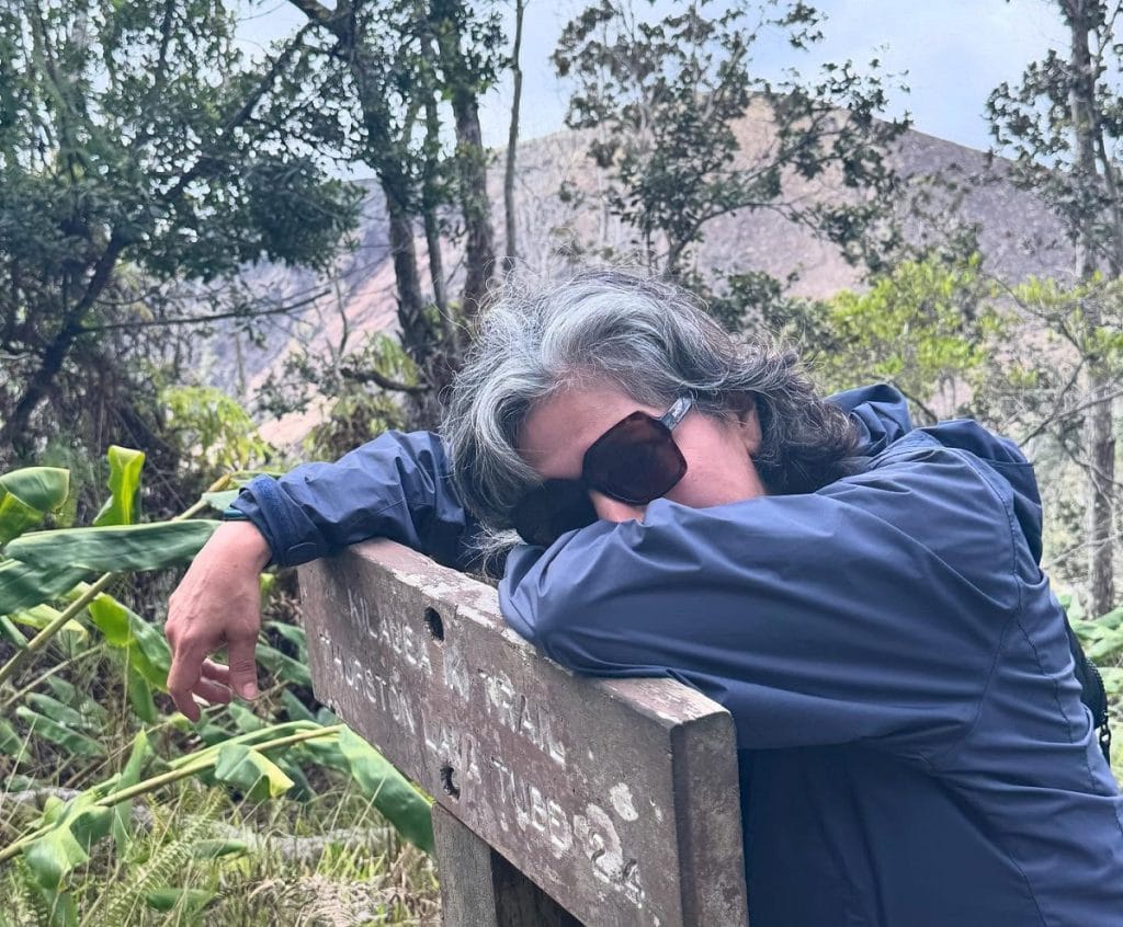 A woman rests on a sign out hiking.