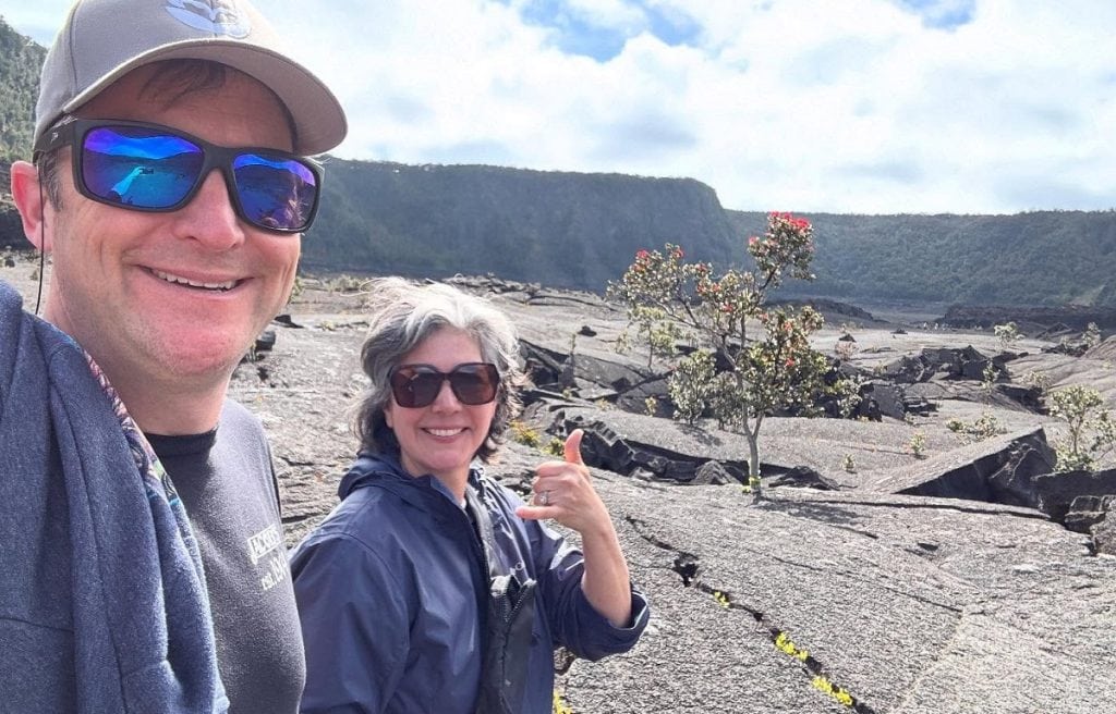 A woman and man are hiking over a lava field.