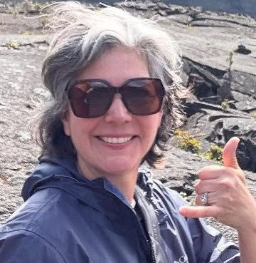 A woman makes a hang-ten sign with her hand while hiking.