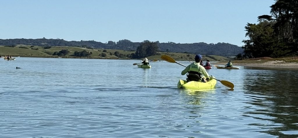 A man in a yellow kayak follows another man on the water.