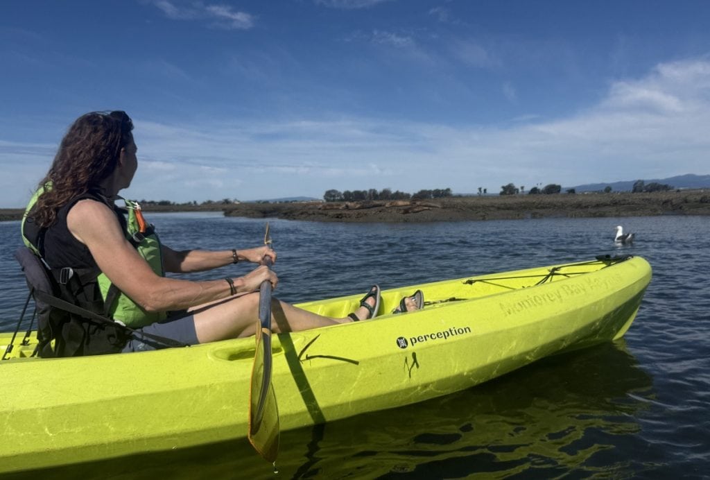 A woman rests in a yellow kayak while looking out at the water.
