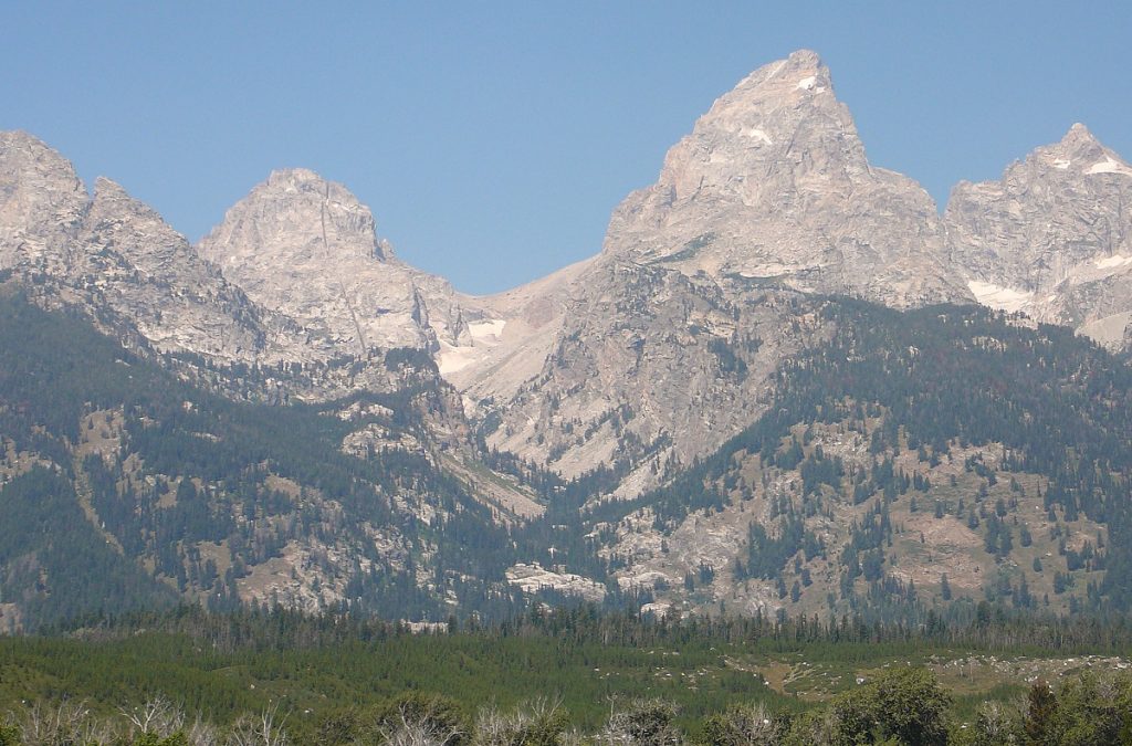 The three peaks of the Teton Range are shown with a clear blue sky.