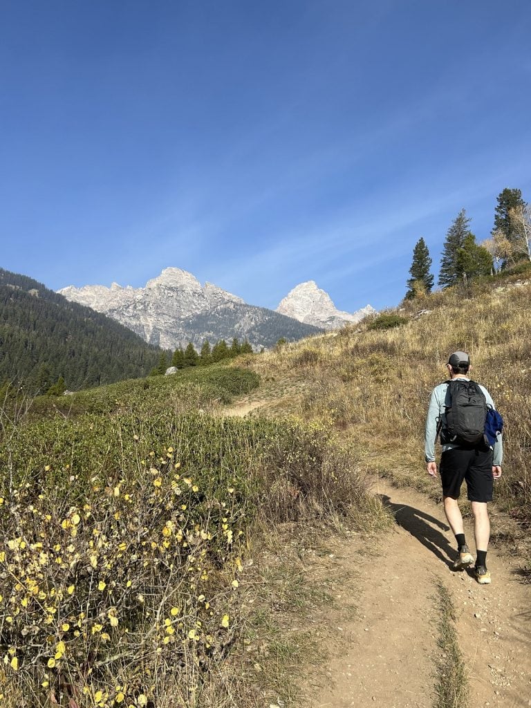 A male hiker looks ahead to see the three peaks of the Teton Range.