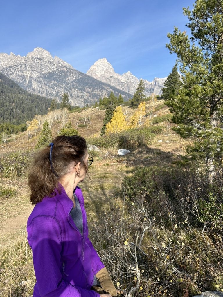A woman looks ahead to see the three peaks of the Teton Range.