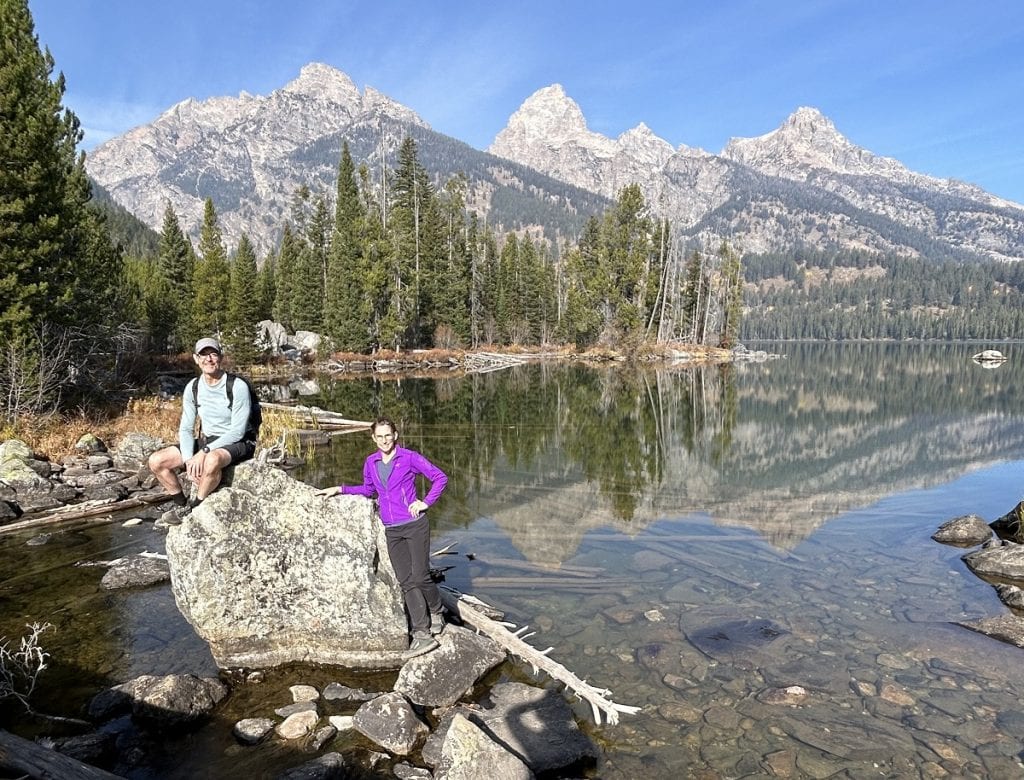 A man and woman stand near a boulder with the three peaks behind them.
