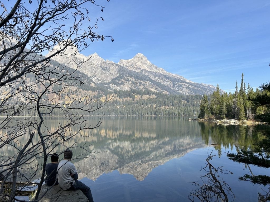 A couple sits on a rock looking at the three peaks across a lake.
