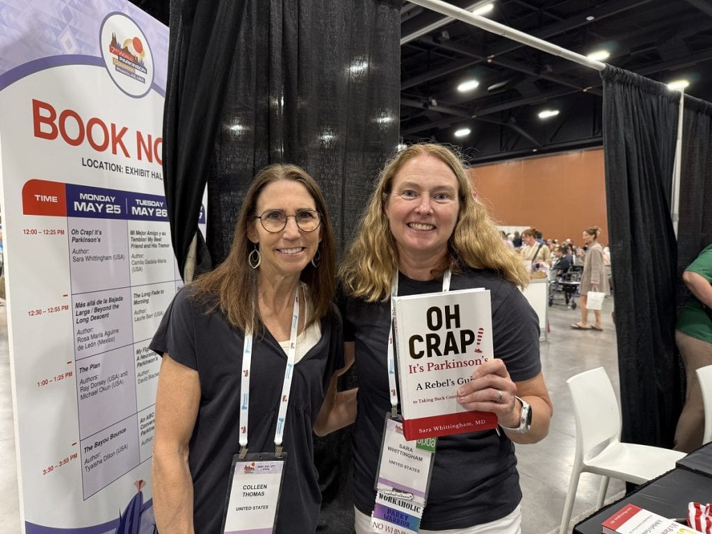 Two women smile for the camera while one holds a book.