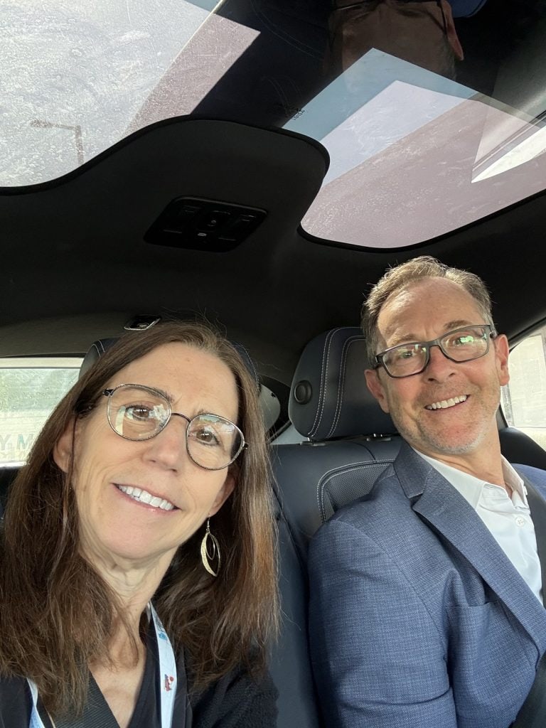 A man and woman sit smiling in the back of a Waymo car.