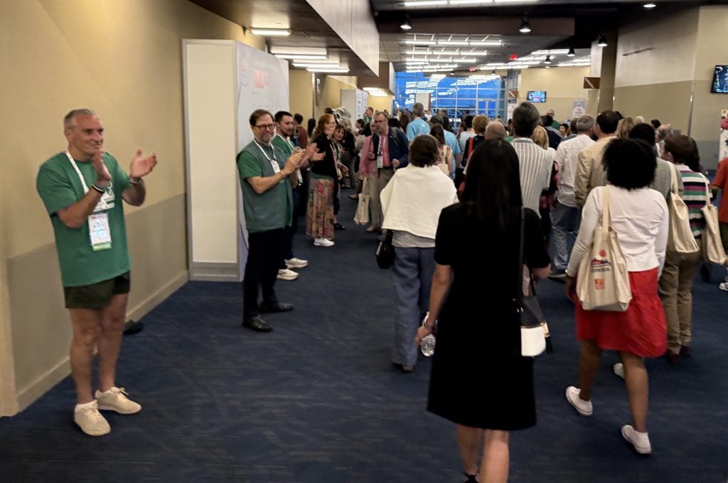 People clap as a crowd moves down a hallway.