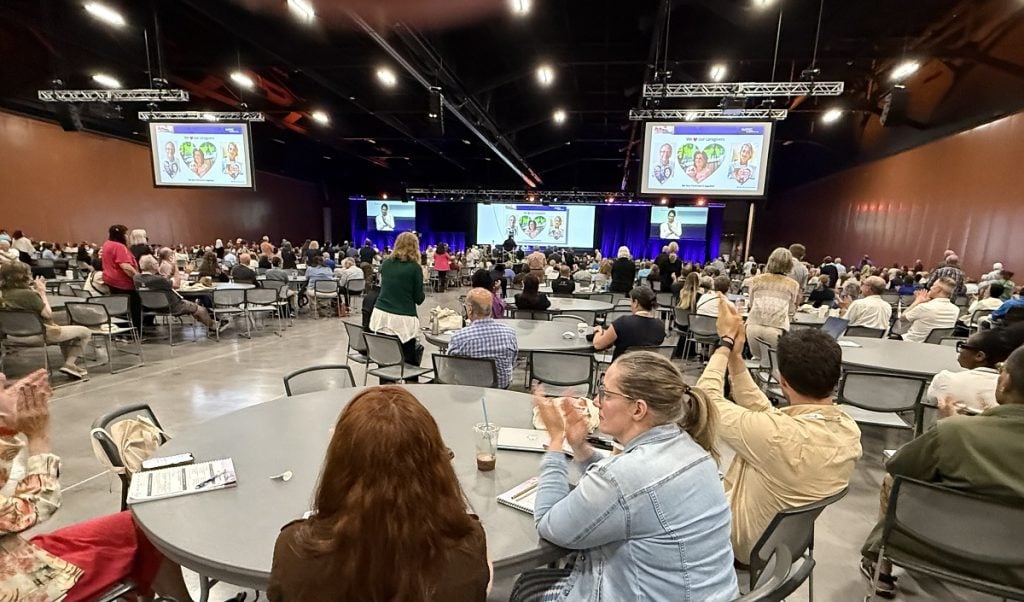People stand up in a large auditorium to be recognized.