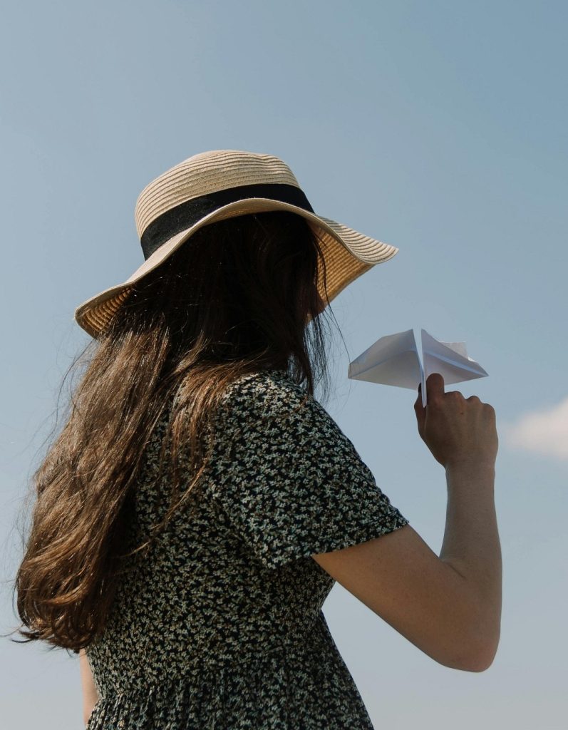 A young woman in a hat gets ready to fly a paper airplane.
