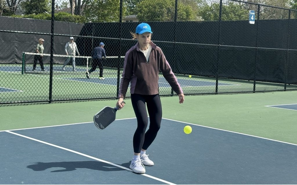 A pickleball player bends down to hit the yellow ball.