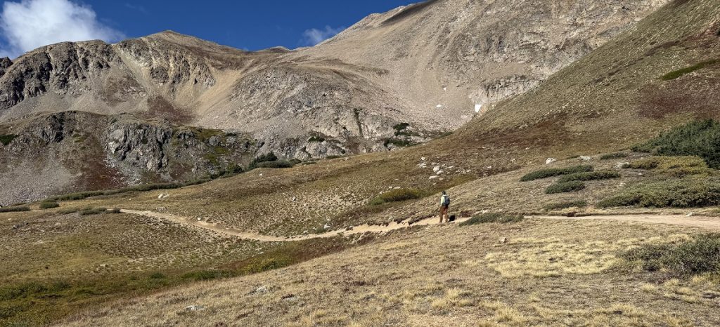 A man hikes over a smooth dirt path toward mountains.