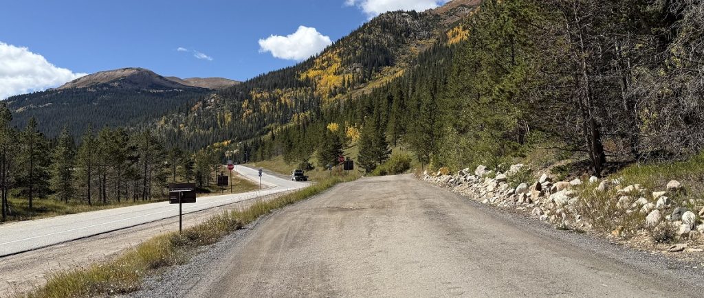 A dirt road runs parallel to a paved one in the mountians.