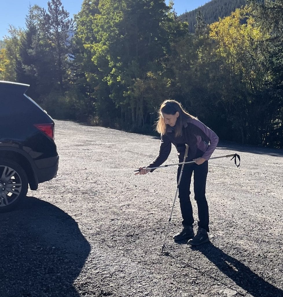 A female hiker adjusts her poles outside a car.