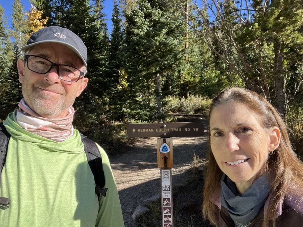 A man and woman stand next to a trailhead sign.