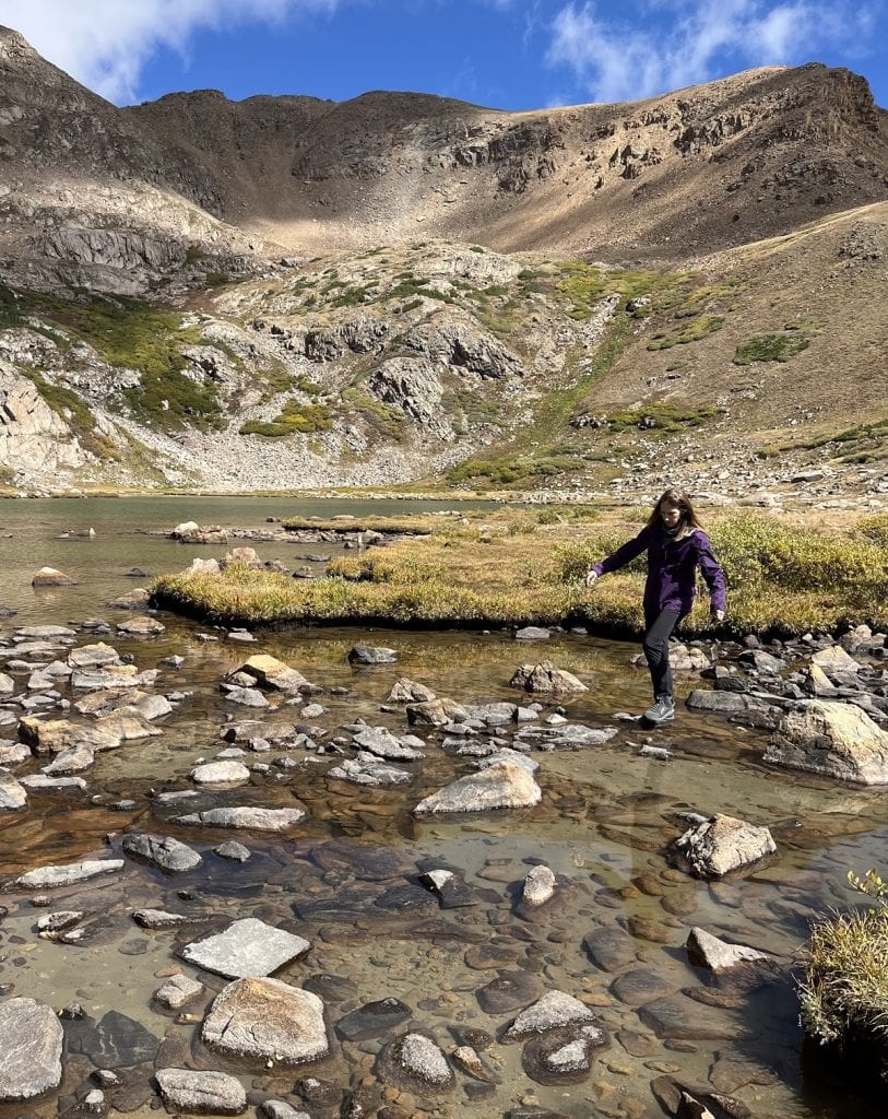 A woman balances on stepping rocks in a shallow lake.