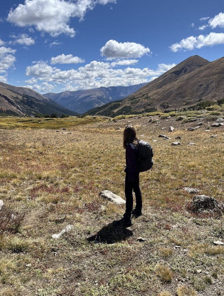 A woman looks out at the mountains with a backpack.