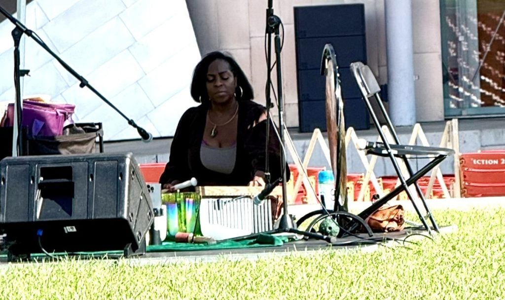A woman sits among musical instruments and a speaker.