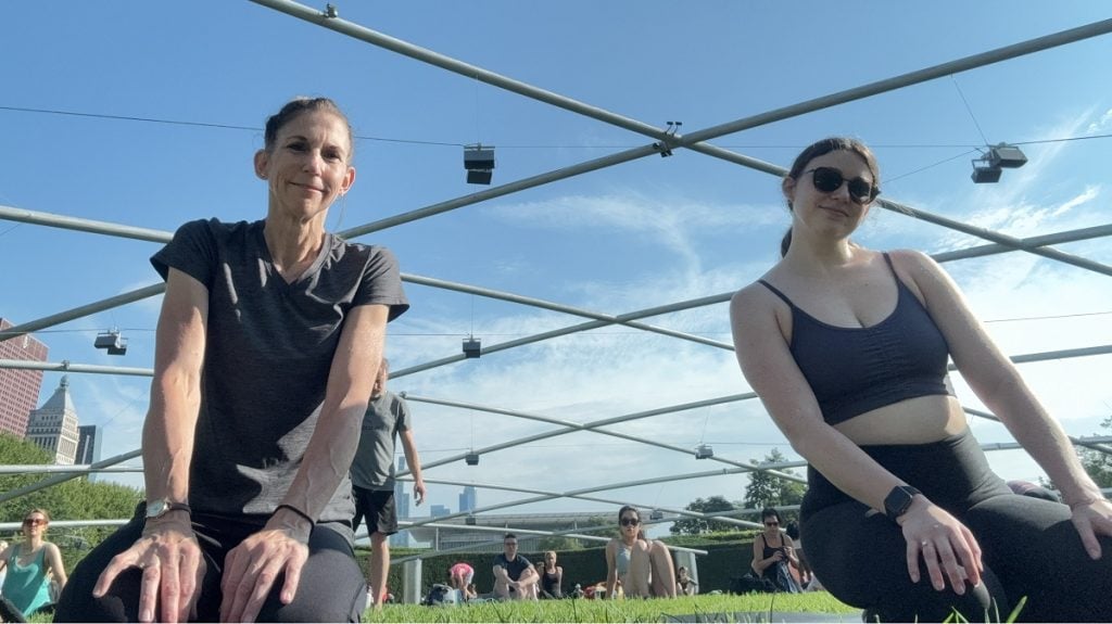 A woman and her adult daughter pose with the blue sky behind them.