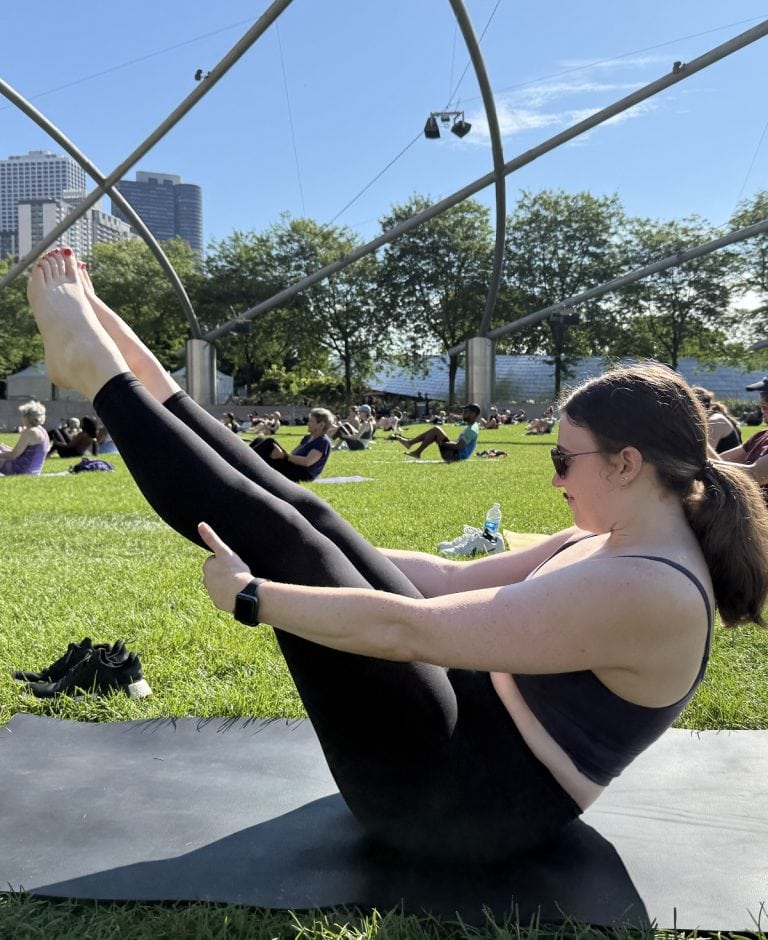 A woman in workout clothes sits with legs up in the air.
