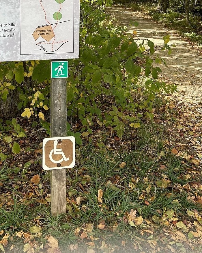 A trail sign shows a "handicapped" symbol on it.
