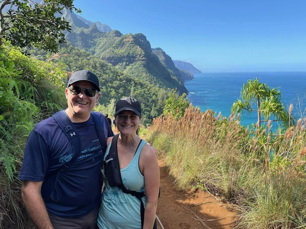 A man and woman are shown on a trail with the ocean in the background.