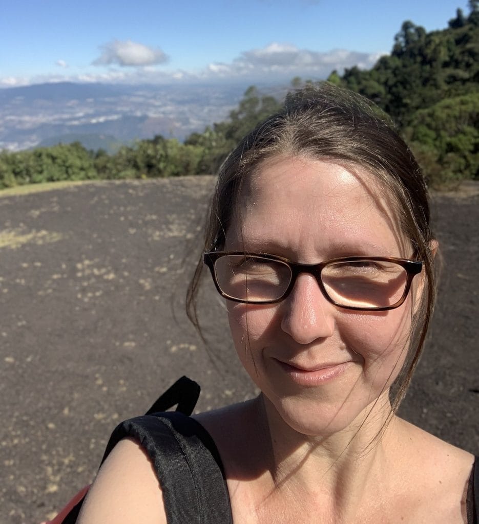 A woman is shown on a hiking trail with the sun shining on her.