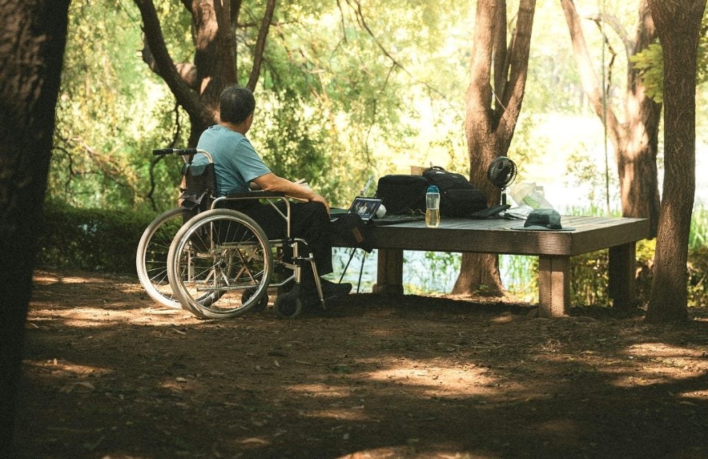 A man in a wheelchair sits at a low outdoor table outside.
