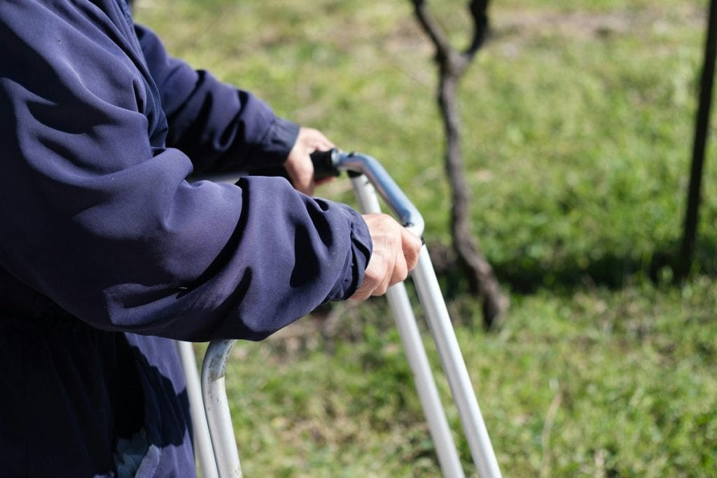 A person clings to a walker while moviing outdoors.