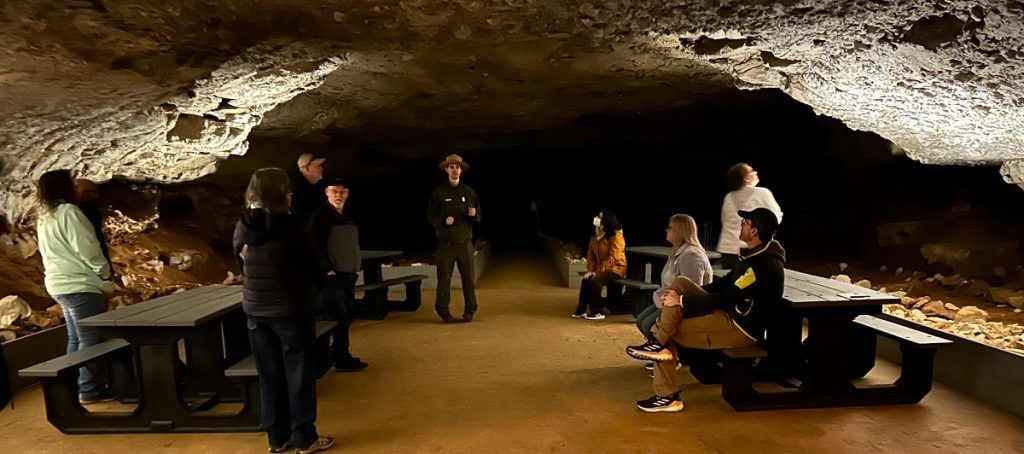 A view inside a cave of a wide open area with people sitting around.