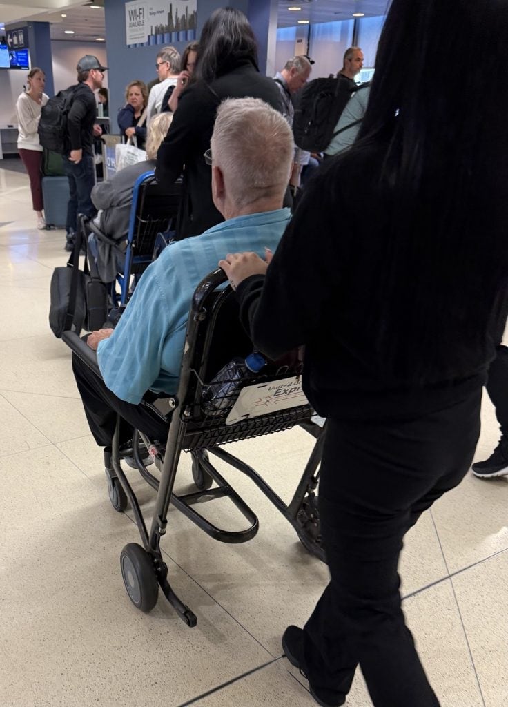 A man in a wheelchair is pushed by an airport worker.
