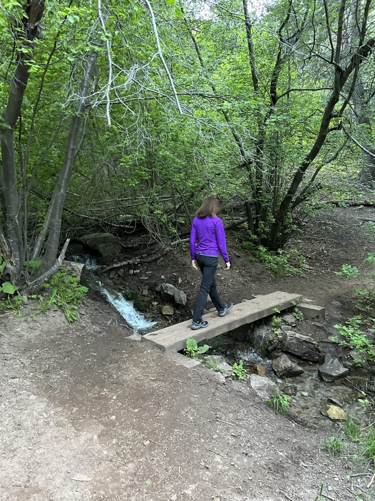 A woman walks over a board plank bridge on a hike.