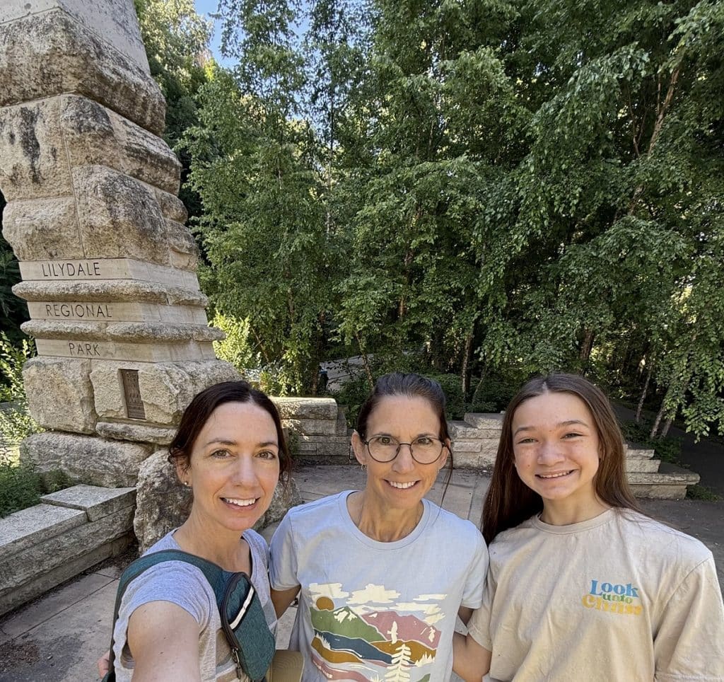 Three people stand in front of a stone sculpture.