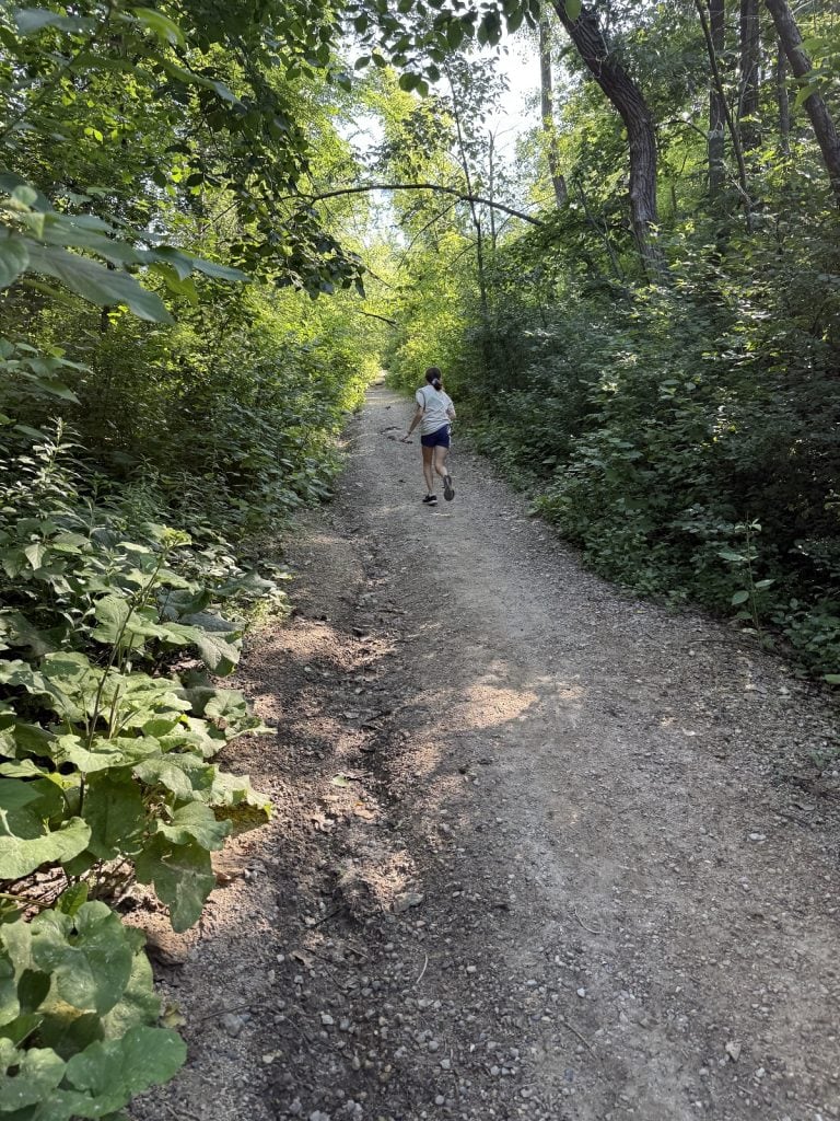 A young girl walks along a dirt path in the woods.