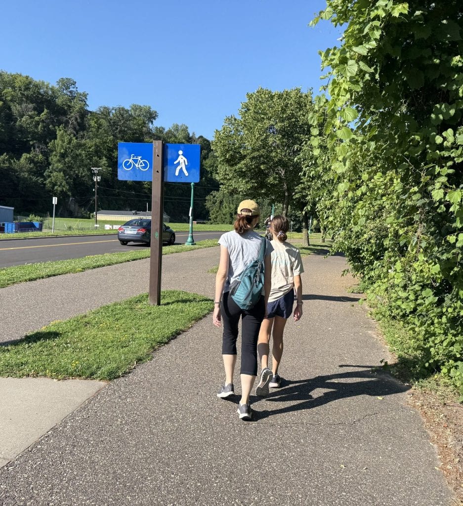 Female hikers walk past a sign showing the way for hikers to go.