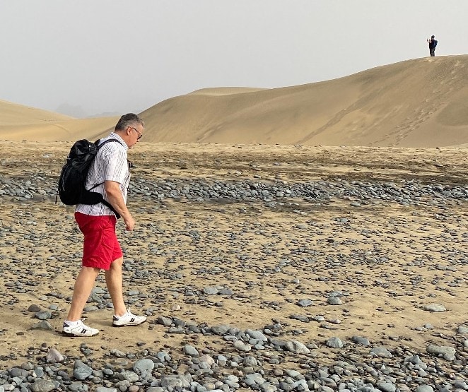 A hiker goes across a dry landscape while his partner waits in the distance.
