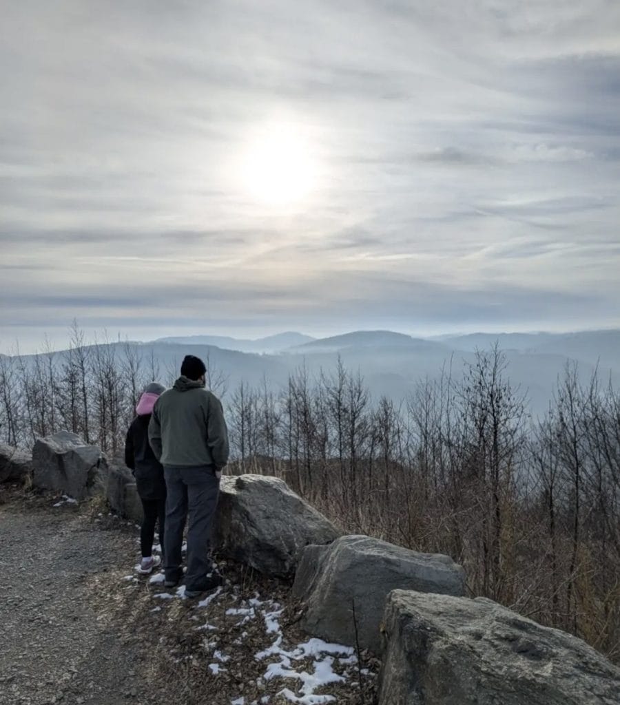 A man and a girl look out at mountains and a sunset.