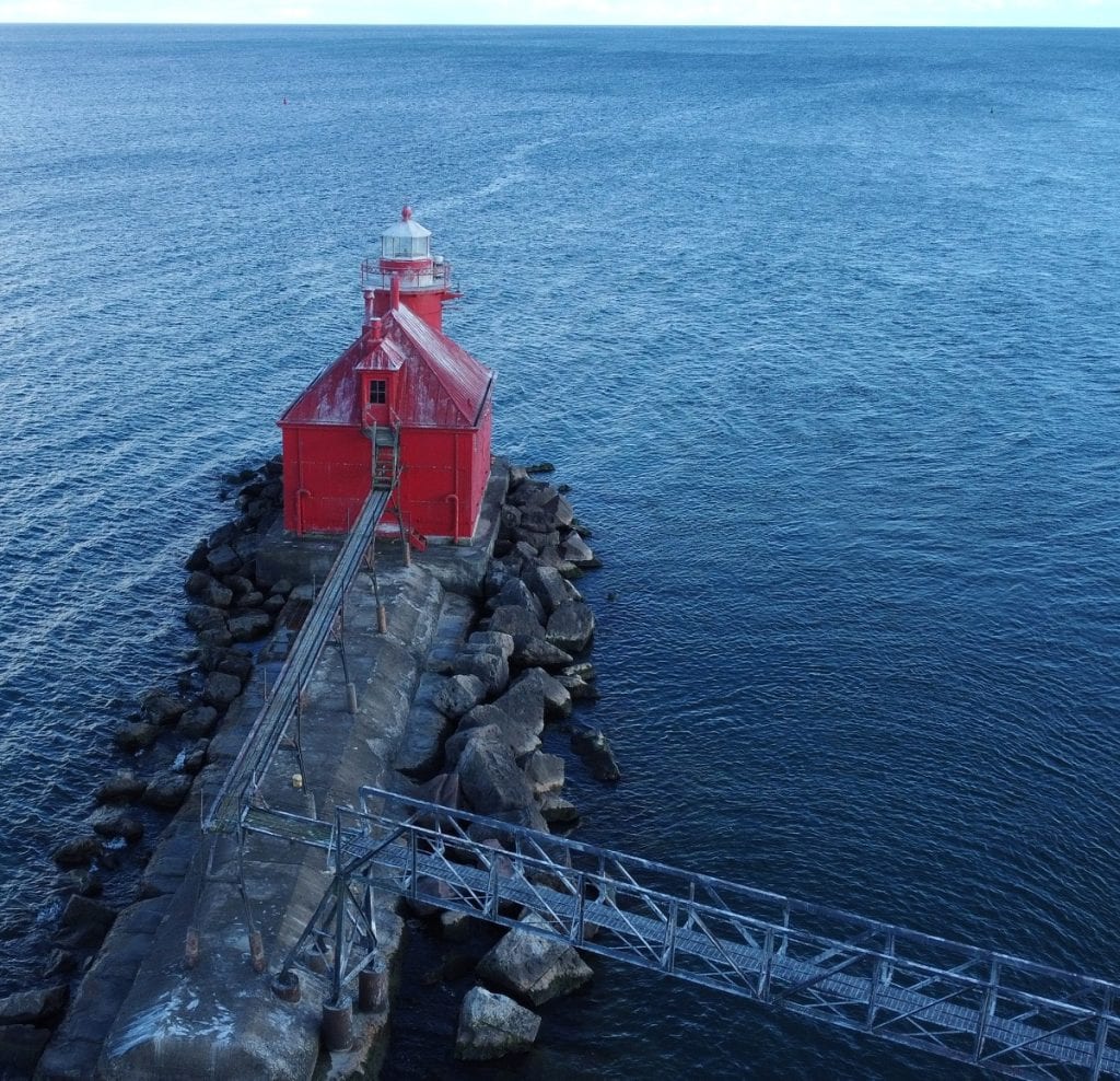 A red painted lighthouse has metal docks leading to it out in the water.