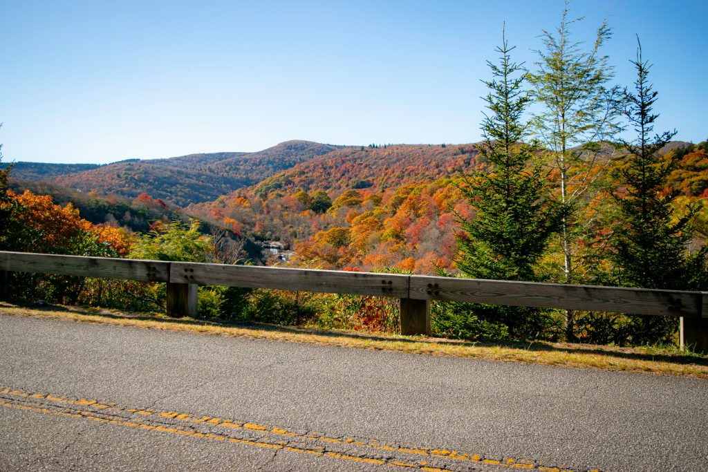 A road with a guard rail goes by a scenic view of fall colors.